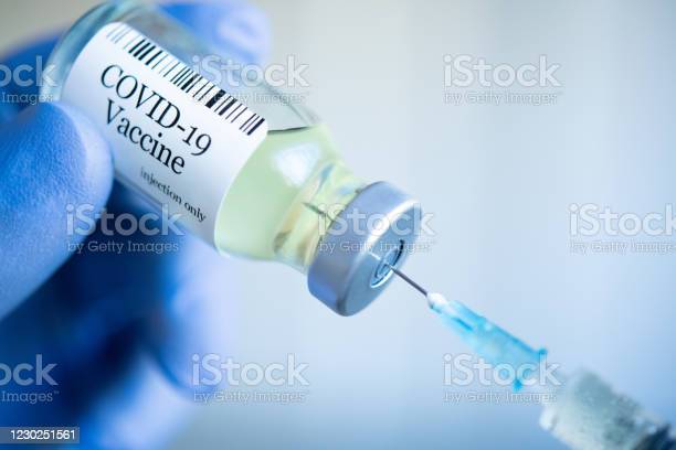 Doctor drawing up Covid-19 vaccine from glass phial bottle and filling syringe injection for vaccination. Close up of hand wearing protective disposable gloves in lab and holding a bottle of vaccination drugs. Hand with blue surgical gloves taking sars-coV-2 vaccine dose from vial with syringe: prevention and immunization concept.